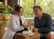 A dentist shows a patient small dental material samples at a warmly lit side table while explaining her findings.